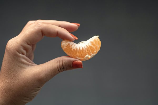 mano femminile che tiene tra le dita uno spicchio d'arancia